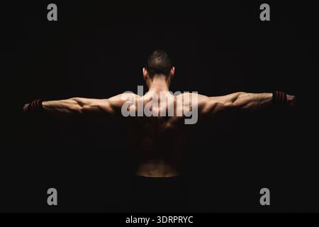 L'homme fort avec les bras tendus dans un cadre sombre montre de la détermination et de la concentration dans la session d'entraînement Banque D'Images