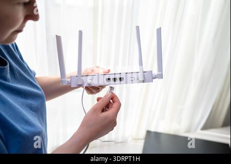 Gros plan d'une personne en chemise bleue connectant un câble réseau à un routeur sans fil. Ce cliché représente l'installation internet à domicile, le tro technique Banque D'Images