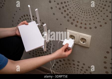 Une personne connecte un routeur Internet sans fil à l'alimentation électrique en branchant l'adaptateur secteur sur une prise murale. Représente les périphériques s. Banque D'Images