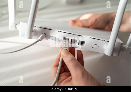 Gros plan détaillé d'une personne connectant un câble réseau à un routeur sans fil doté d'antennes. Concept de configuration Internet haut débit, su technique Banque D'Images