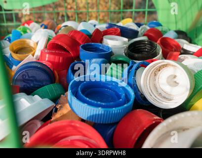 Vue rapprochée de bouchons de bouteilles en plastique colorés à l'intérieur d'un conteneur en maille pour la collecte des déchets recyclables, mettant en évidence la durabilité Banque D'Images