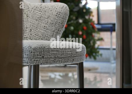 La chaise est assise devant un sapin de Noël. La chaise est blanche et noire et a un motif sur elle. L'arbre est décoré d'ornements et de lumières. Banque D'Images