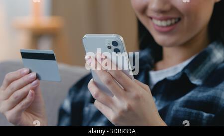 Heureuse femme asiatique souriante client dame inconnue assise sur le canapé à la maison tenant la carte de crédit utilisez l'application payante de téléphone mobile en ligne fille coréenne féminine Banque D'Images