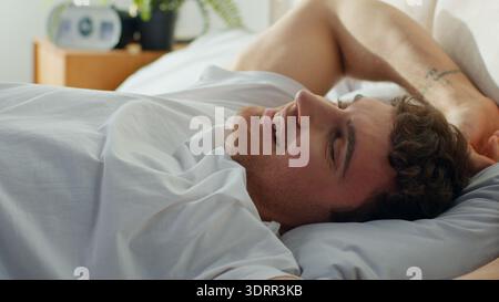 Homme européen réveillant le lit à la maison étirant le sourire homme caucasien gars profiter du bon matin confort chambre confortable week-end repos hôtel orthopédique Banque D'Images