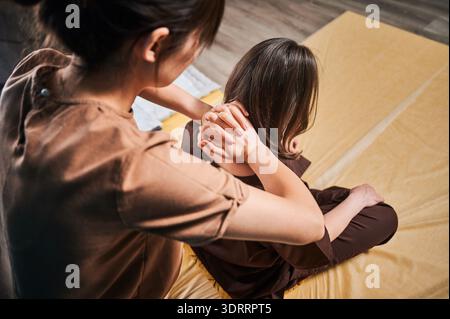 Masseuse faisant massage yoga thaïlandais. Vue rognée de thérapeute de femme faisant le traitement de massage traditionnel pour la patiente féminine. Client assis sur tapis, profitant d'un massage des mains dans une atmosphère calme. Gros plan. Banque D'Images