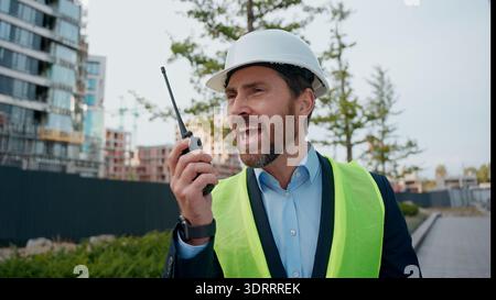 Homme caucasien agacé dans l'ingénieur casque criant talkie walkie trouble construire travailleur agressif en colère fou furieux architecte entrepreneur criant Banque D'Images