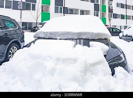 Gros plan d'une voiture sombre moderne complètement enterrée sous la neige fraîche profonde avec un épais chapeau de neige sur le toit après un blizzard hivernal massif Banque D'Images