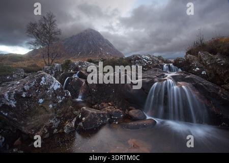 Petites cascades coulant sur des rochers sombres avec montagne et ciel orageux dans les Highlands écossais, Glen Etive Banque D'Images