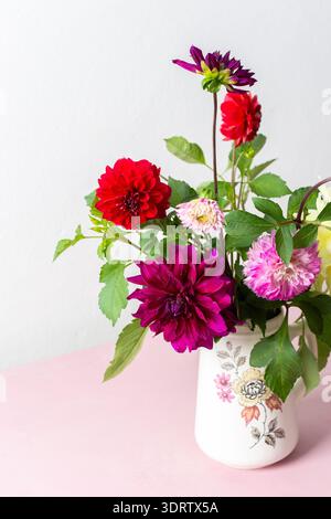 Un vase contient une variété de fleurs fraîches avec différentes couleurs. Les fleurs sont placées sur une table rose. Derrière le vase se trouve un mur Uni dans un roo lumineux Banque D'Images