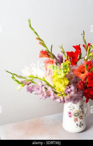 Un vase contient une variété de glaïeules colorés, y compris des fleurs rouges et blanches. L'arrangement se trouve sur une surface propre, ajoutant une touche de nature au Banque D'Images