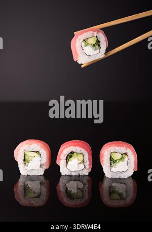 Délicieux Sushi Rolls placés sur une table noire avec des baguettes tenant un morceau de Sushi Banque D'Images