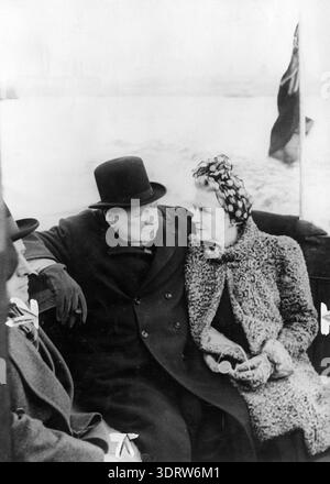 Dans cette photographie franche en noir et blanc des années 1940, Sir Winston Churchill et son épouse Clementine Churchill sont vus ensemble, probablement à bord d'un navire en Nouvelle-Zélande. Churchill, portant son chapeau melon signature, regarde vers sa femme, qui est ornée d'un foulard à motifs et d'un manteau texturé, reflétant un moment d'intimité partagée au milieu de leur vie publique. Banque D'Images
