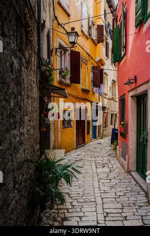 Vue des bâtiments vibrants peints dans des tons chauds jaunes et rouges, bordant une étroite rue pavée dans la vieille ville, créant une scène charmante, Rovinj, Banque D'Images