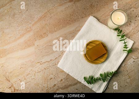Vue de dessus de serviette blanche avec savon sur plat en bois et bougie allumée sur marbre beige, décoré avec eucalyptus. Fond de spa de bien-être minimal avec copie Banque D'Images