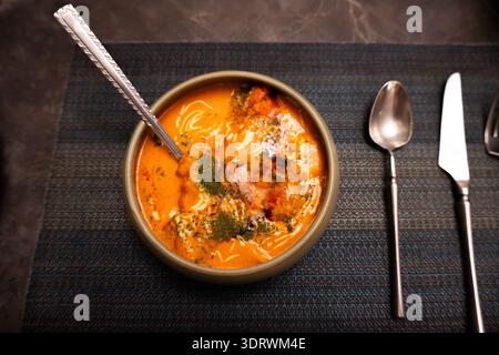 Soupe turque aux lentilles dans un bol en céramique avec cuillère sur une nappe texturée foncée, garnie d'herbes et de yaourt Banque D'Images