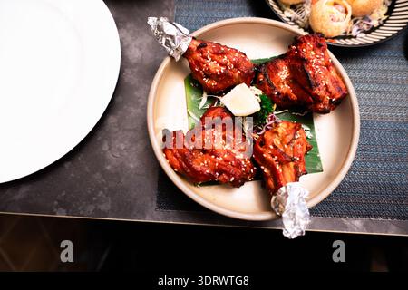 Pilons de poulet tandoori indien sur une assiette garnie de feuilles avec beurre, servis à la table du restaurant Banque D'Images