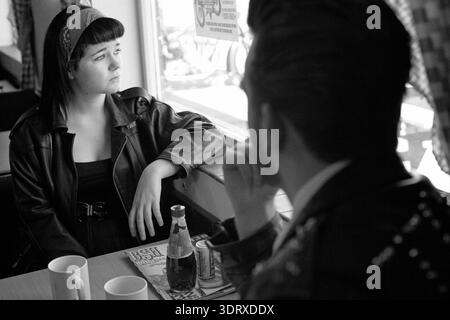 Jeune couple nostalgique dans un café de style restaurant américain, cadre d'inspiration vintage avec la femme regardant soigneusement par la fenêtre. Banque D'Images