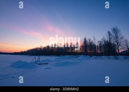 Coucher de soleil sur le lac Inari gelé avec des arbres couverts de neige en Laponie, Finlande près d'Ivalo Banque D'Images