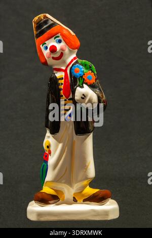 Gros plan d'une bouteille miniature en céramique de liqueur en forme de clown de cirque coloré sur fond de tissu gris foncé. Banque D'Images