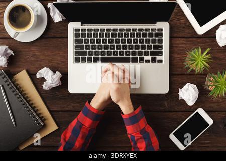 La configuration du travail montre des mains réfléchissant sur l'ordinateur portable avec du café et des papiers sur la table en bois Banque D'Images