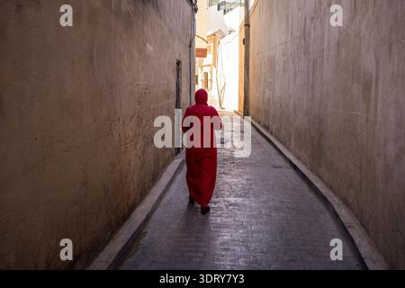 Une vue arrière saisissante d'une femme portant une djellaba rouge traditionnelle alors qu'elle marche dans une ruelle étroite dans le quartier historique de la médina de Casablanca. T Banque D'Images
