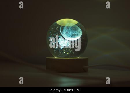 Un orbe de verre incandescent sur une base en bois révèle une méduse 3D et des bulles, à l'intérieur la nuit. La lumière bleu turquoise projette des étincelles, avec un éclairage doux et shal Banque D'Images