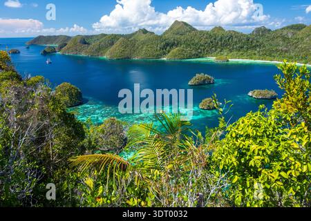 Vue panoramique depuis le sommet du Mont Pindito dans le lagon Wayag surplombant l'eau bleue, les récifs coralliens, un voilier et un paysage verdoyant Raja Ampat, Indonésie Banque D'Images