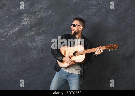 Homme joue de la guitare dans un cadre de studio portant des lunettes de soleil dans des vêtements décontractés Banque D'Images