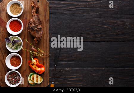 Diverses épices et légumes disposés sur une planche en bois avec de la viande grillée Banque D'Images
