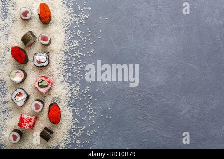 Rouleaux de sushi disposés sur fond gris avec du riz dispersé à côté d'eux Banque D'Images