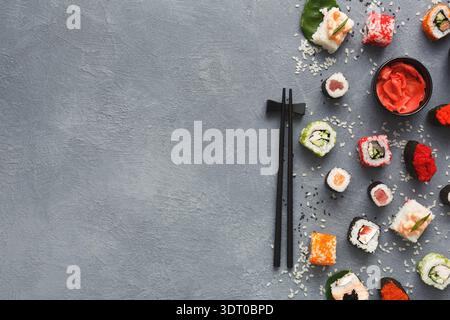 Divers morceaux de Sushi disposés sur une surface grise avec des baguettes et du gingembre mariné Banque D'Images