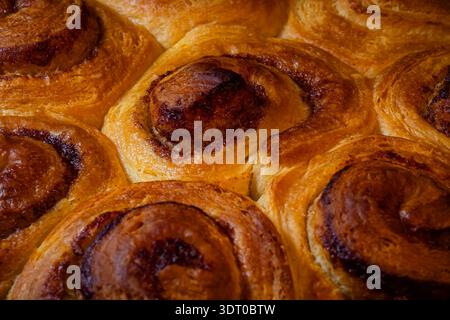 Gros plan de petits pains à la cannelle fraîchement cuits montrant une croûte dorée, une texture riche et des tourbillons de fourrage à la cannelle Banque D'Images
