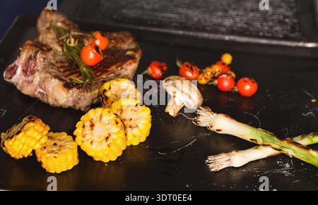 Collage d'aliments grillés montrant des légumes et de la viande sur une assiette noire lors d'un rassemblement d'été Banque D'Images