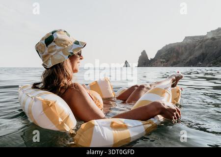 Femme Raft gonflable Sea relaxation - Une femme portant un chapeau et des lunettes de soleil se détend sur un radeau gonflable dans la mer, avec des falaises rocheuses dans le Banque D'Images