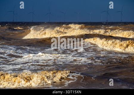 Marteler les vagues de la mer d'Irlande avec des éoliennes à l'horizon Banque D'Images