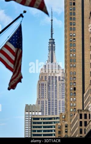 Les drapeaux agitent dans le vent alors que l'Empire State Building se dresse à Manhattan, New York par temps clair. Banque D'Images