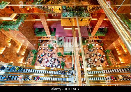 Les gens s'assoient et parlent dans l'atrium de la Trump Tower tandis que certains marchent dans les escaliers. L'espace a de nombreuses plantes et surfaces réfléchissantes. Banque D'Images