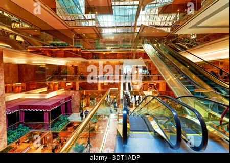 Les gens marchent et interagissent dans l’atrium de la Trump Tower tandis que les escaliers mécaniques montent et descendent. L'espace dispose de grands murs et de grandes fenêtres. Banque D'Images