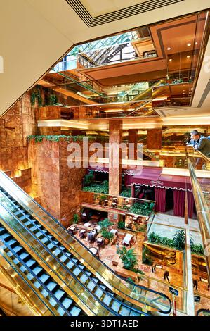 Les gens marchent dans l'atrium Trump Tower à Manhattan. Le grand espace présente des détails en verre et en marbre, avec des boutiques et des coins salon. Banque D'Images