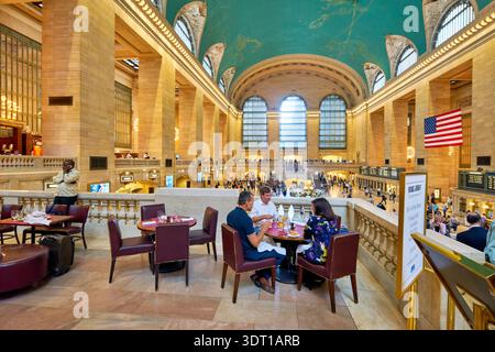Les gens mangent dans un restaurant à l'intérieur de Grand Central terminal. La station animée a beaucoup de visiteurs et un haut plafond. Banque D'Images