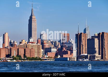 La vue montre les gratte-ciel de Manhattan avec l'Empire State Building sous un ciel dégagé. Les bâtiments bordent le front de mer avec de l'eau au premier plan. Banque D'Images