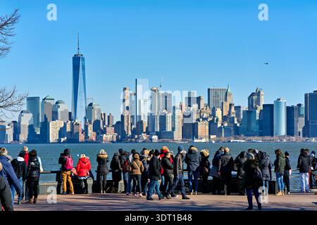 Des foules de touristes se tiennent sur Liberty Island, admirant la vue sur les gratte-ciel de Manhattan à travers l'eau par temps clair. Banque D'Images