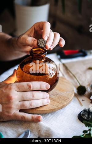 Les mains tiennent le petit kenzan au-dessus du vase en verre rond. Art traditionnel ikebana, grenouille fleur kenzan, arrangement floral japonais, esthétique minimaliste Banque D'Images