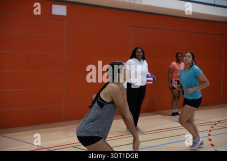 Diverses coéquipières féminines pratiquant le volley-ball dans le gymnase en vêtements de sport avec entraîneur tenant le volley-ball Banque D'Images