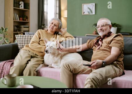 Couple caucasien senior se relaxant sur canapé avec chien dans le salon confortable Banque D'Images