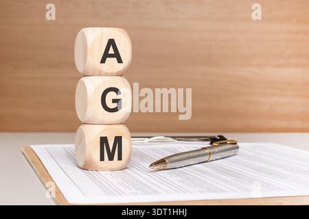 Cubes de bois naturel empilés verticalement avec les lettres A, G, M assis sur des papiers à côté d'un stylo sur un bureau. composition épurée et minimaliste Banque D'Images