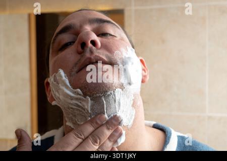 Homme appliquant de la mousse à raser sur son visage, se préparant au rasage et au toilettage quotidien Banque D'Images