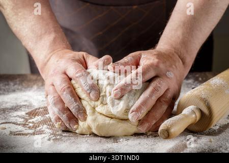 Mains masculines préparant la pâte pour le pain ou d'autres pâtisseries gros plan sur une table en bois avec de la farine Banque D'Images