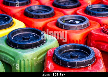 Gros plan de plusieurs jerry Cans en plastique colorés avec des bouchons à vis noirs en rouge, vert, orange et jaune, pris d'en haut. Banque D'Images