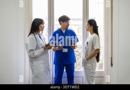 Une équipe médicale diversifiée composée de deux médecins et d'une infirmière a entamé une discussion au sein d'un hôpital. Les professionnels portent des gommages et des blouses de laboratoire, holdi Banque D'Images